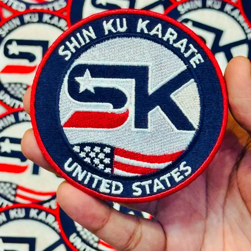 Hand holding a round Shin Ku Karate custom embroidered patch to show size and stitching detail.