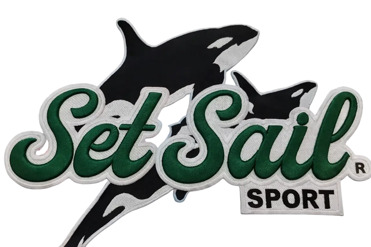 Large custom embroidered logo patch reading 'Set Sail Sport' with green script lettering and black whale silhouette on white backing.